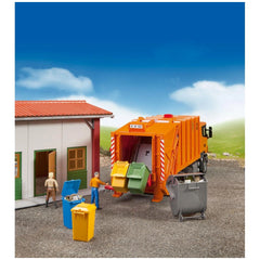 Toy garbage truck with colorful bins beside a small building, featuring miniature figures simulating waste collection.