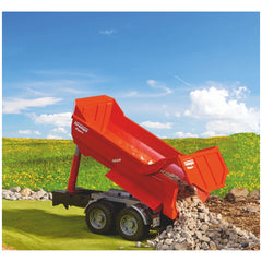Red Bruder Krampe Tandem Halfpipe Tipping Trailer unloading rocks on green field under blue sky.