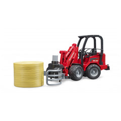 Red Bruder Schäffer Compact Loader with bale gripper holding a yellow bale.