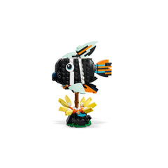 Colorful tropical fish model made of LEGO bricks, featuring a black body, orange and blue fins, and a playful eye, perched on a green base surrounded by yellow flowers.