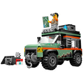 LEGO® City Off-Road Mountain Truck in vibrant green and orange, featuring a minifigure on the roof holding binoculars and a map. The truck showcases rugged tires, a working winch, and roof storage boxes, positioned next to a tool set for adventurous play.