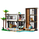 Modern two-story LEGO Creator beach house construction set, featuring palm trees, a pool, and two mini-figures enjoying outdoor activities.