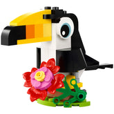 Colorful Lego Tropical Toucan model with a vibrant yellow beak, black body, and white chest, surrounded by a pink flower and green leaves.