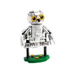 Posable white snowy owl figure, Hedwig, perched on a black sign reading "Privet Drive," set on a green base with small yellow flowers.
