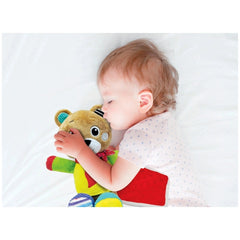 Baby Clementoni Bob The Bear is a plush teddy bear held by a sleeping child in a colorful outfit on a soft surface.
