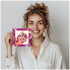 Brown-haired person in a white shirt creating a colorful unicorn diamond painting on a purple cardboard.