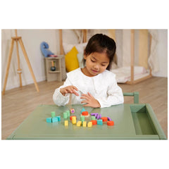 Eichhorn Games Staple Game features a girl sorting colorful blocks on a light green table in a minimalist playroom.