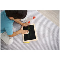 Eichhorn Small Blackboard - A child engages with a drawing tablet on the floor, surrounded by a pencil, fostering creativity.