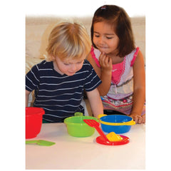 Gowi Cooking Set Vienna with green, red, and blue bowls, and red and green spoons on a white tabletop with two children.