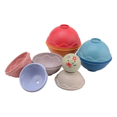 Happy World stacking balls in pink, blue, and orange matte bowls with glossy interiors on a white surface.