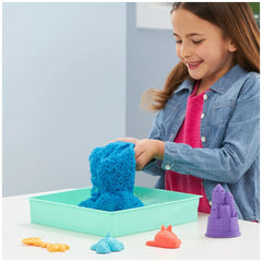Kinetic Sand Sandbox Set features a smiling girl engaged with colorful fluffy sand materials on a green tray at a white table