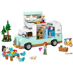 LEGO Friends Friendship Camper Van Adventure set featuring a light blue camper van, two minidolls playing with colorful dishes, a ferret, and camping accessories. A tree set and a bicycle are nearby, enhancing the outdoor adventure theme.