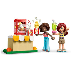 Two LEGO Friends minidolls, one holding popcorn and the other a drink, stand beside a popcorn machine with movie-themed accessories.