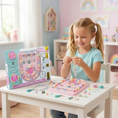 Young girl in blue shirt and jeans smiles while holding colorful beads on a pink tray atop a white table in a playful room.