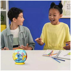 Ravensburger 3D Puzzle Ball featuring Disney's Stitch is being enjoyed by two smiling children at a table with craft supplies