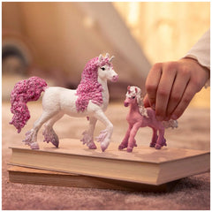 Pink and white unicorn figurine with a pink mane and tail, held above a smooth, light-colored hardcover book.