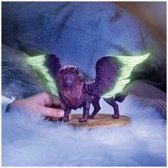 Moon Lion figurine with wings in purple hues, held by a hand against a soft, blurred indoor backdrop.