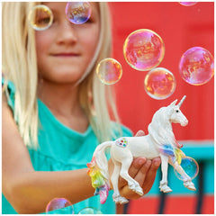 Rainbow Love Unicorn Stallion figurine held by a young girl in a light blue top, set against an outdoor background.
