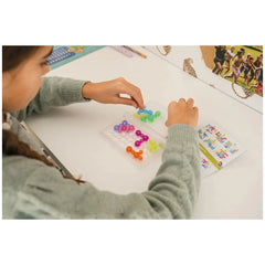 Smart Games IQ Bubbles showcases a child using tweezers to pick colorful beads from a transparent tray on a white table.
