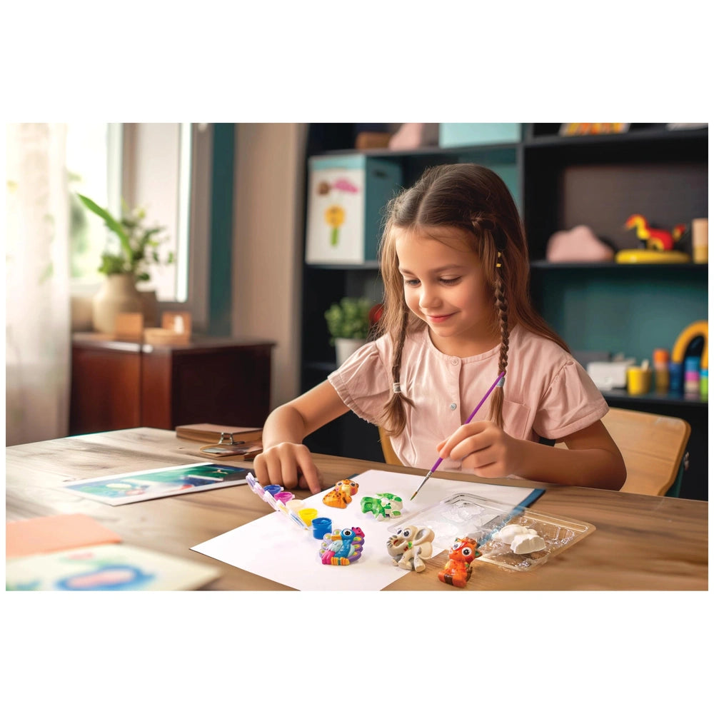 4M Mould & Paint Googly Eyes Animals craft kit on a wooden table with a girl in a pink shirt using crayons and scissors.