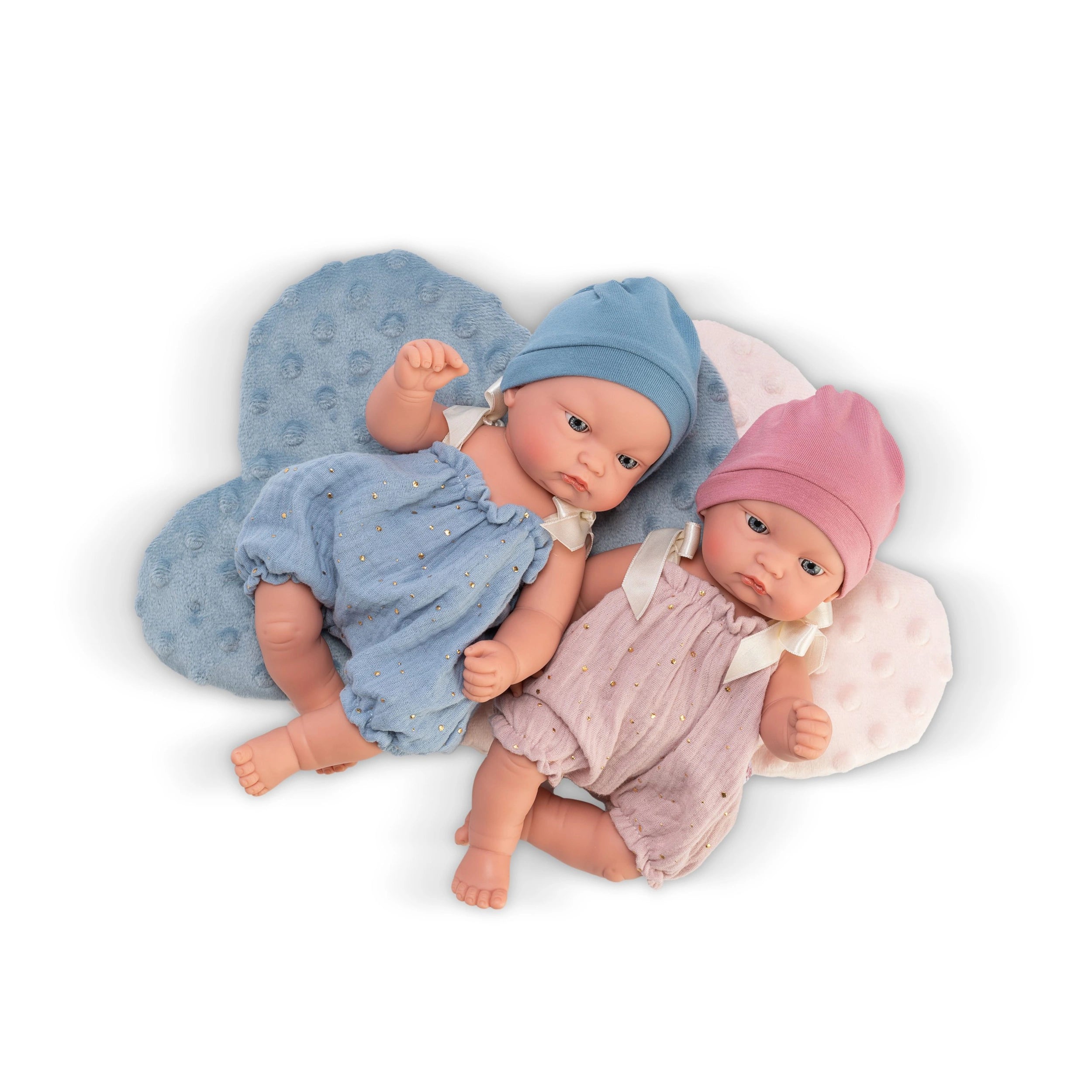 Two ASI Dolls with blue and pink rompers and matching hats, lying on cloud-shaped cushions.
