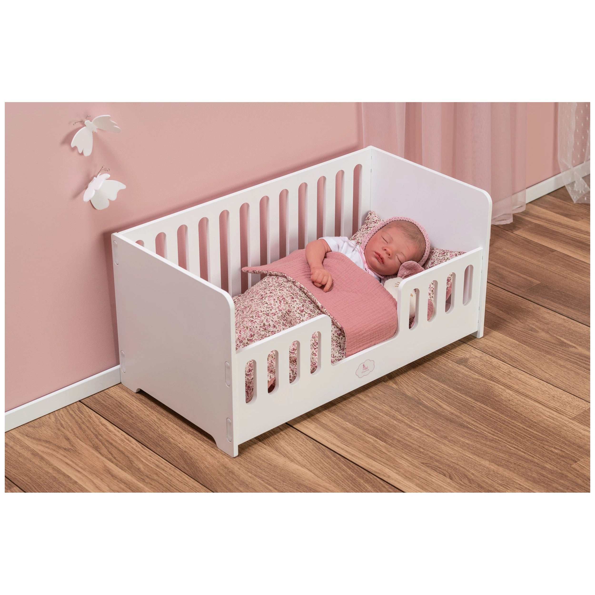 White wooden cradle with a sleeping doll, pink bedding, and floral patterns, set against a soft pink wall with butterfly decor.