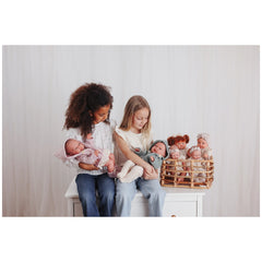 Two children sitting on a white table holding Maria dolls from ASI Dolls Iris Collection, with more dolls in a basket beside them.