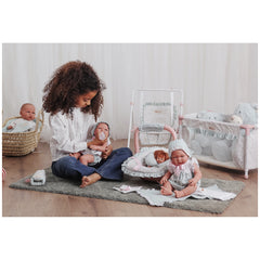 Young girl feeding a doll with a bottle, surrounded by several dolls and the ASI Dolls Maxi-Cosi with neck cushion.
