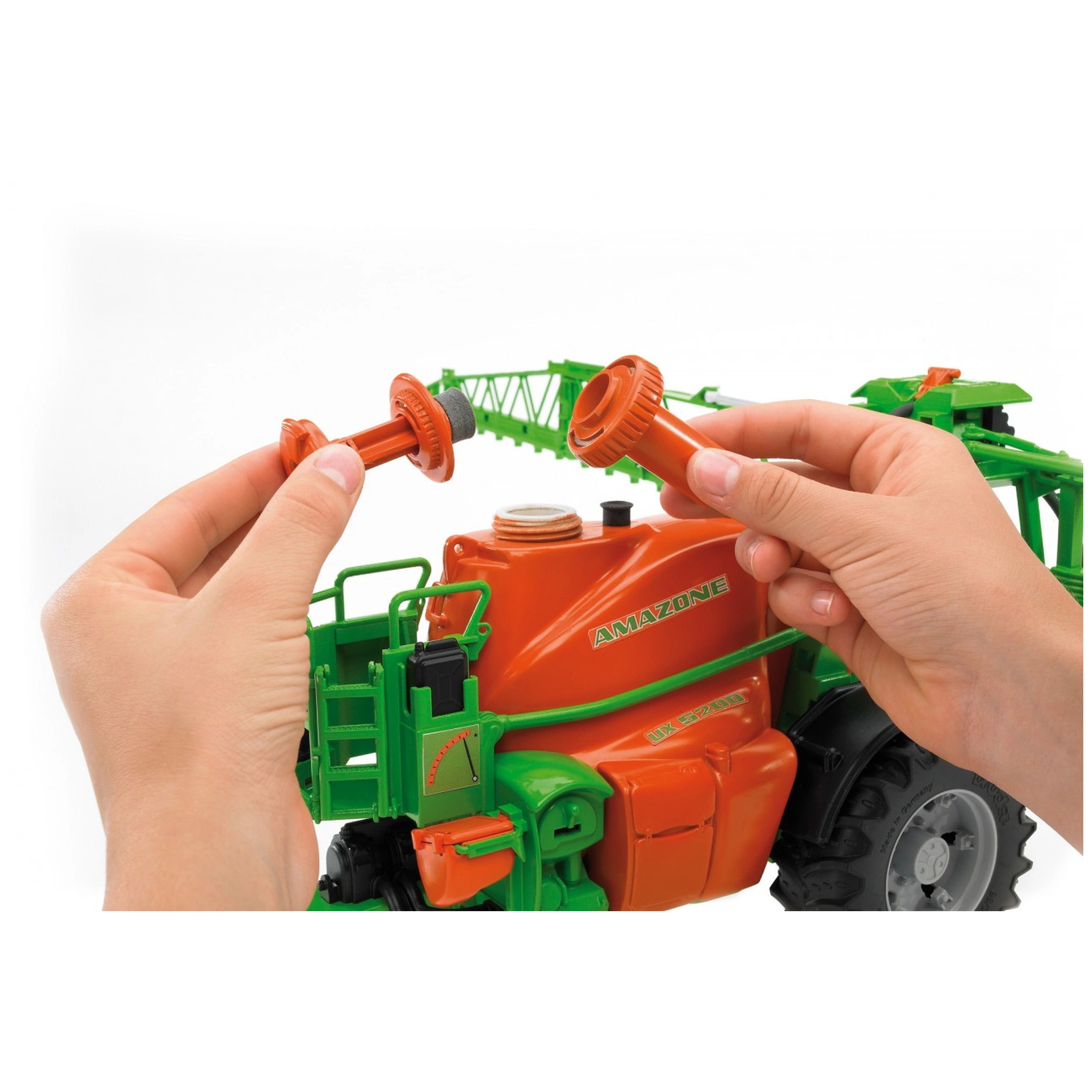 Hands assembling the orange and green Bruder Amazone UX 5200 field sprayer toy, showing realistic detailing.