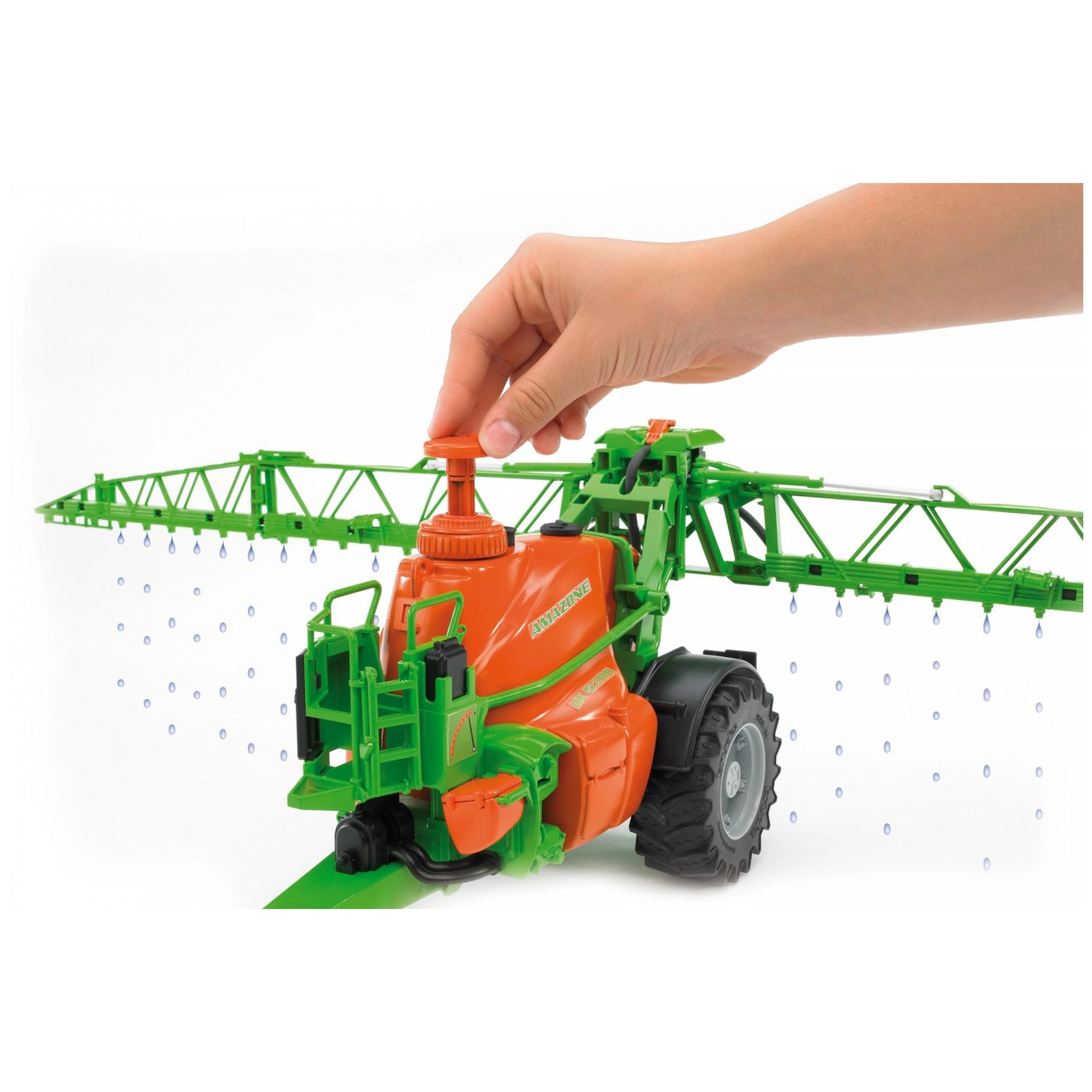Hand adjusting the orange and green Bruder Amazone UX 5200 field sprayer toy with sprinkling water effect.