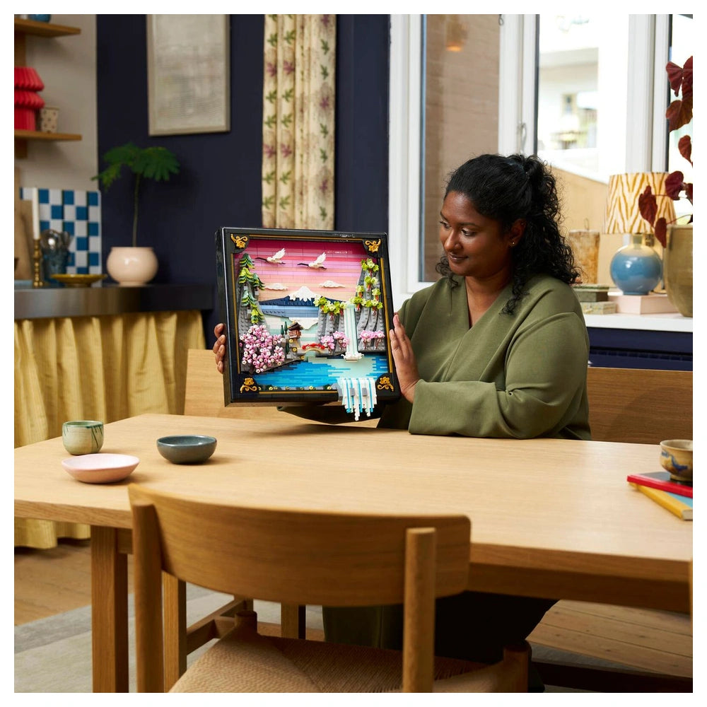 LEGO Art set featuring a Japanese Cherry Blossom landscape displayed by a smiling person at a modern dining table.
