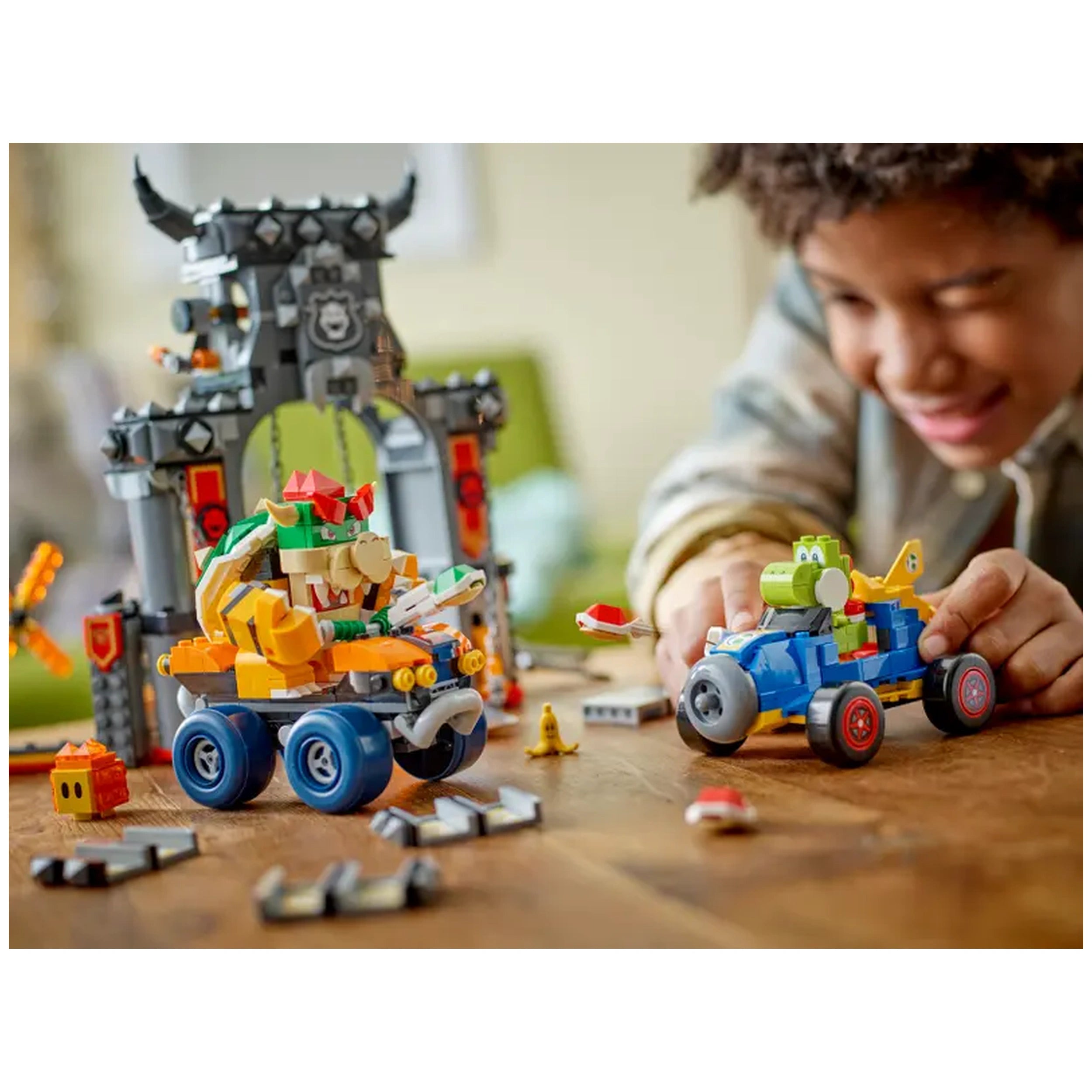 A boy joyfully interacts with LEGO Bowser's Castle, featuring Bowser in a vehicle and Yoshi in a colorful kart. Bright assembly pieces and playful game elements create a vibrant scene.
