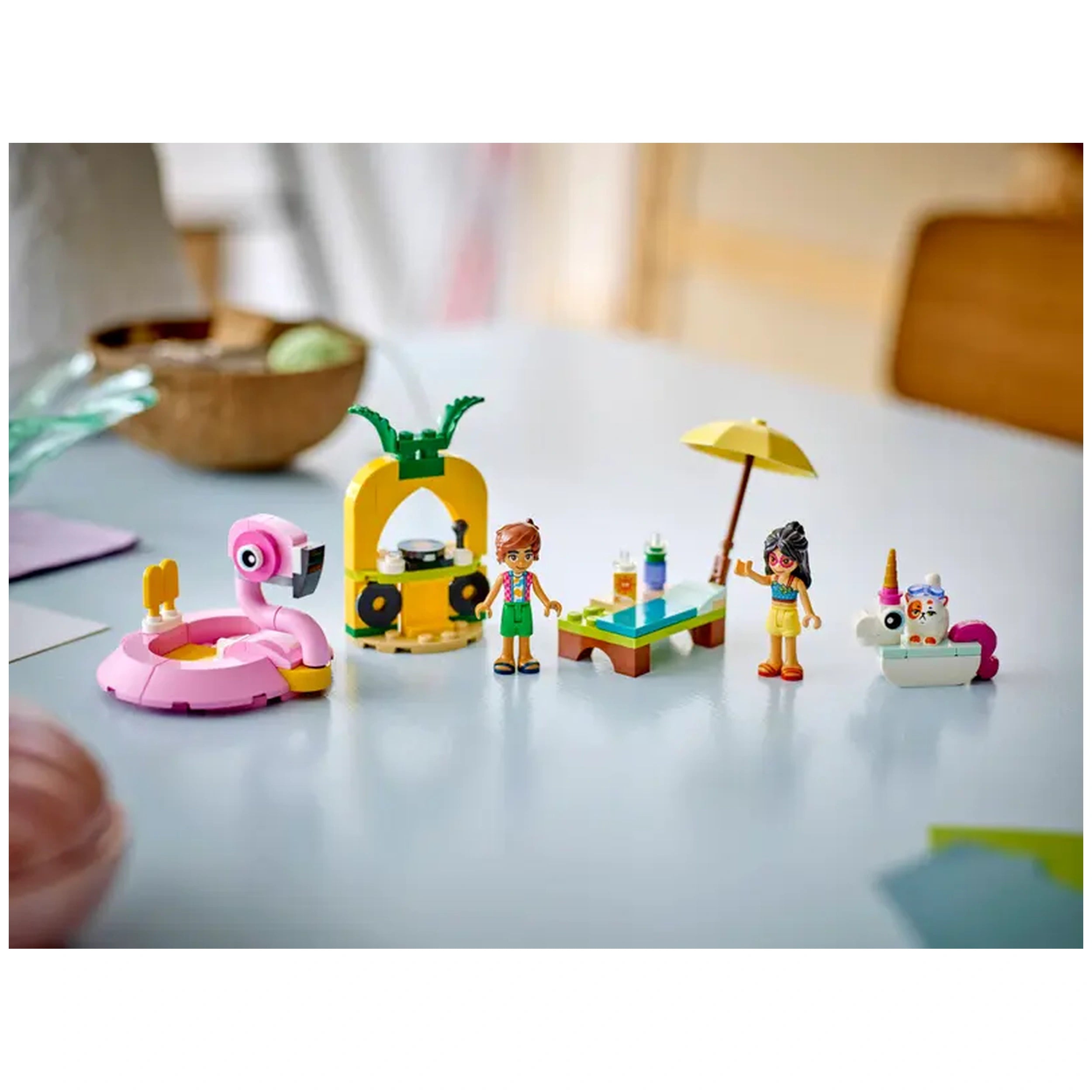 Colorful LEGO Friends set featuring a pink flamingo floatie, two minidolls, a table with drinks, and a unicorn floatie in a playful pool party scene.