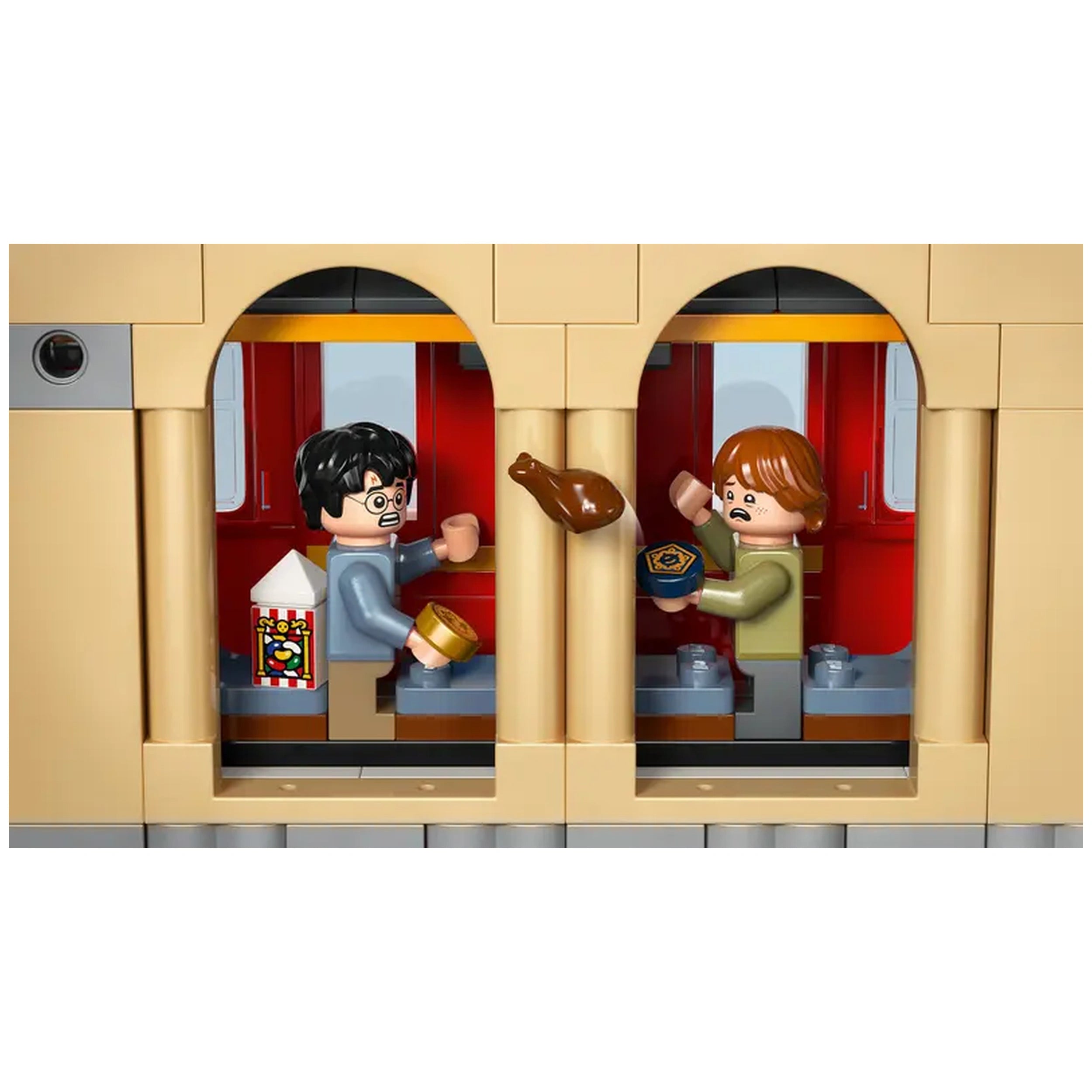 Harry Potter and Ron Weasley LEGO minifigures sit inside a Hogwarts Express train compartment, surrounded by red and tan decor. Harry looks surprised, holding a food item, while a brown food piece is flying towards him. A snack box with colorful stripes is visible beside Harry. Ron, wearing a green sweater, reaches out with a shocked expression, holding a blue container. The scene captures a moment of playful chaos in the wizarding world.