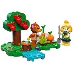 LEGO® Animal Crossing™ set featuring a brown bear character and Isabelle. They stand beside a green tree with red apples, watering carrots and pumpkins in a vibrant garden setting.