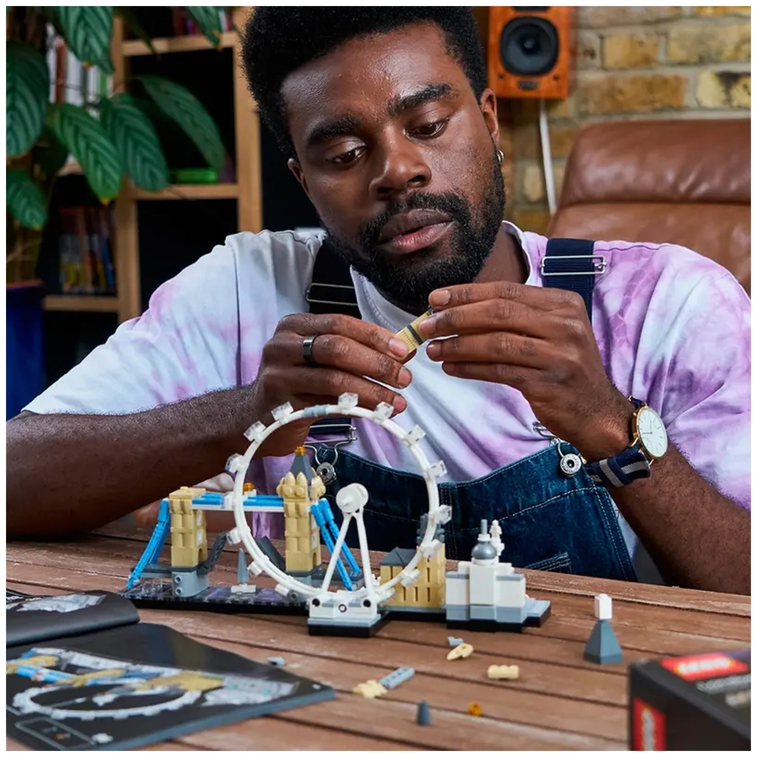 A focused individual assembles LEGO Architecture London set on a wooden table, surrounded by iconic landmarks like the London Eye and Big Ben, engaged in building.