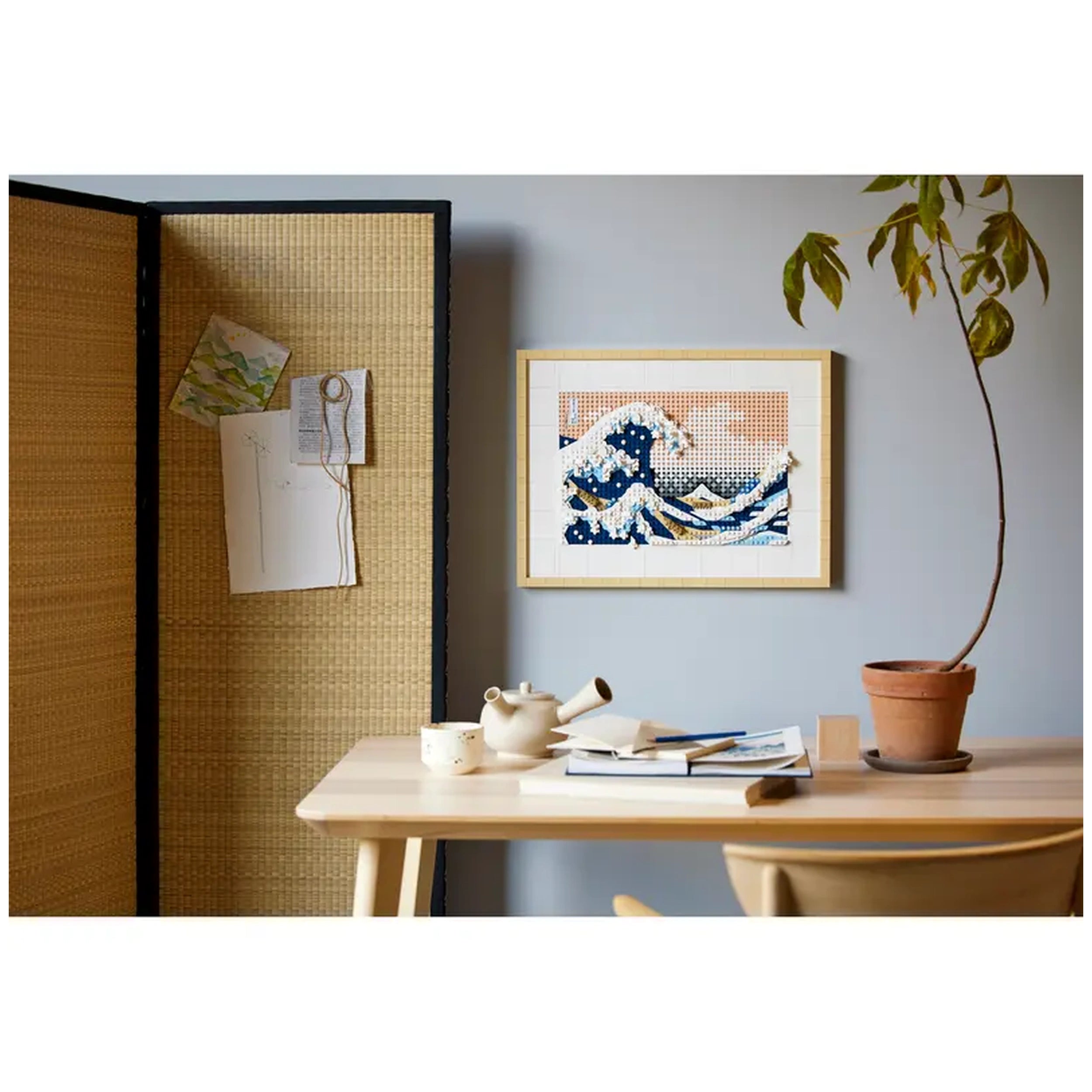 LEGO® Art display of Hokusai’s The Great Wave in a modern room, framed with a pale wood border, beside a desk with a teapot and books.