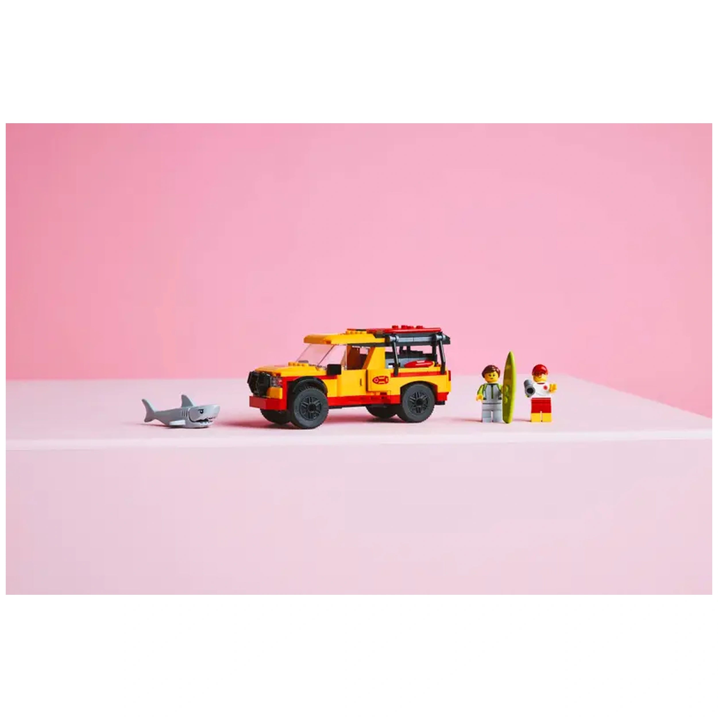 LEGO® City Lifeguard Beach Rescue Truck in vibrant yellow, with two minifigures and a shark figure on a pink backdrop.