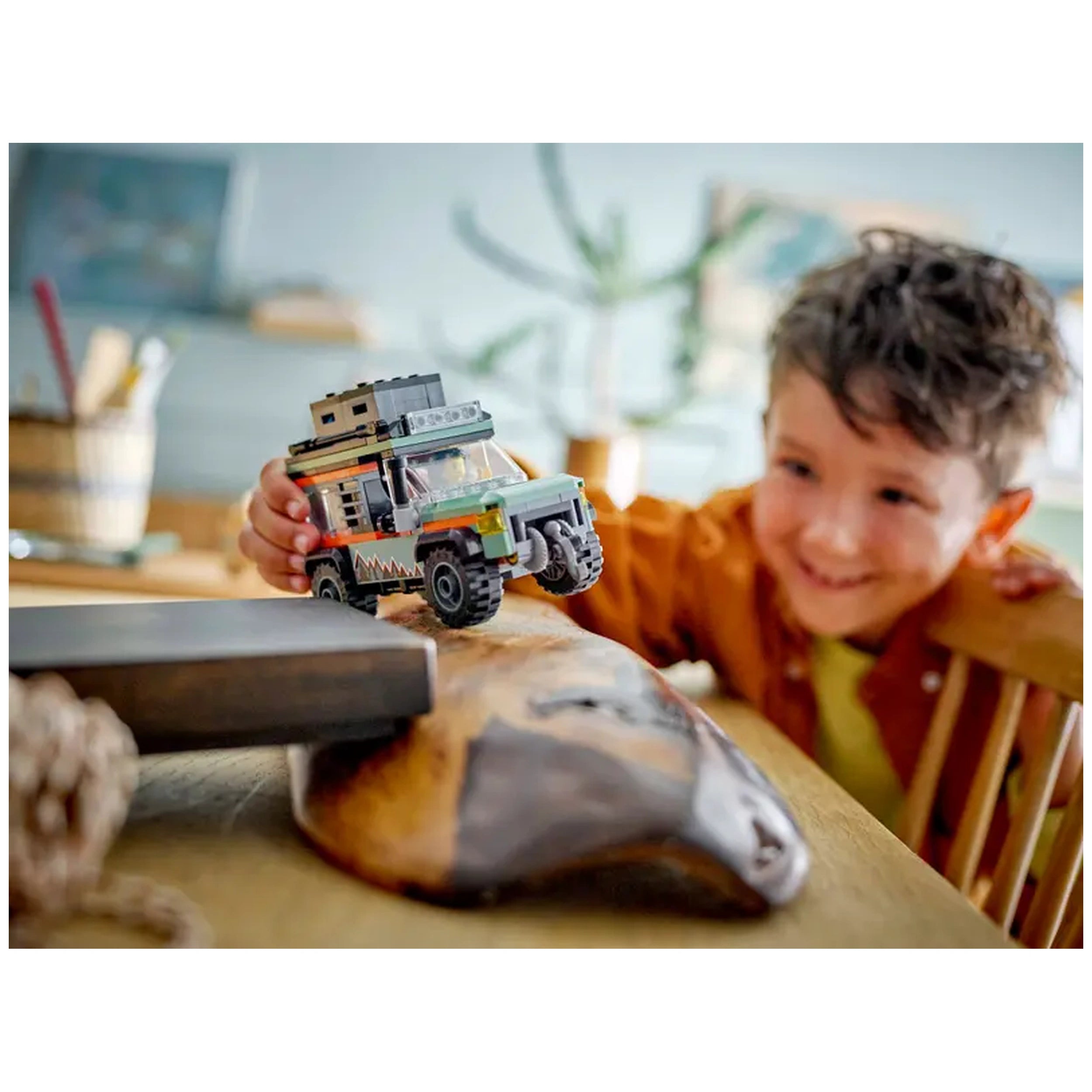 A child joyfully plays with the LEGO® City Off-Road Mountain Truck on a wooden table, showcasing vibrant colors and rugged details.