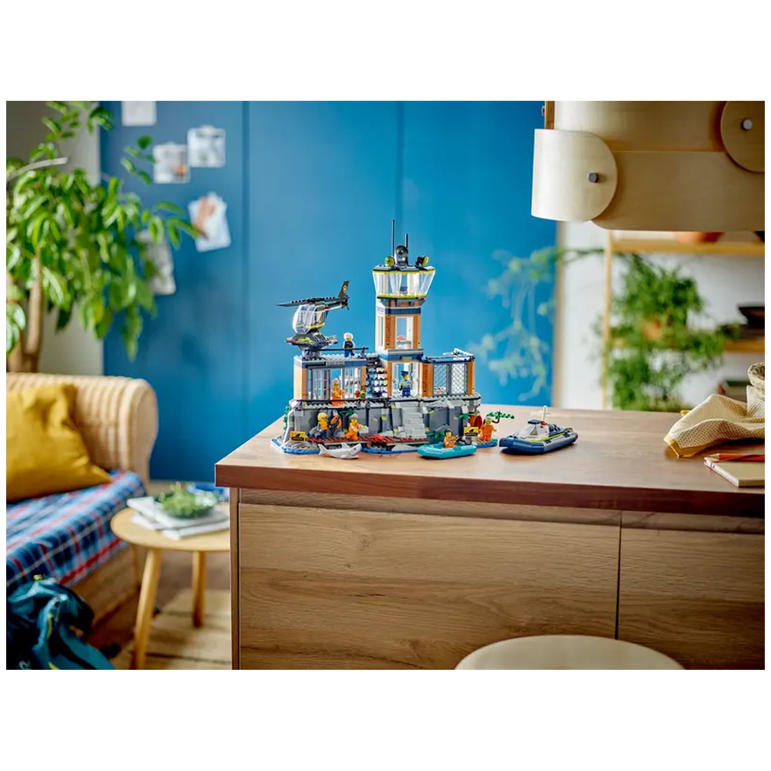 LEGO® City Police Prison Island set on a wooden table, featuring a detailed cliffside prison, officers, and escape boats, surrounded by foliage and cozy furniture.
