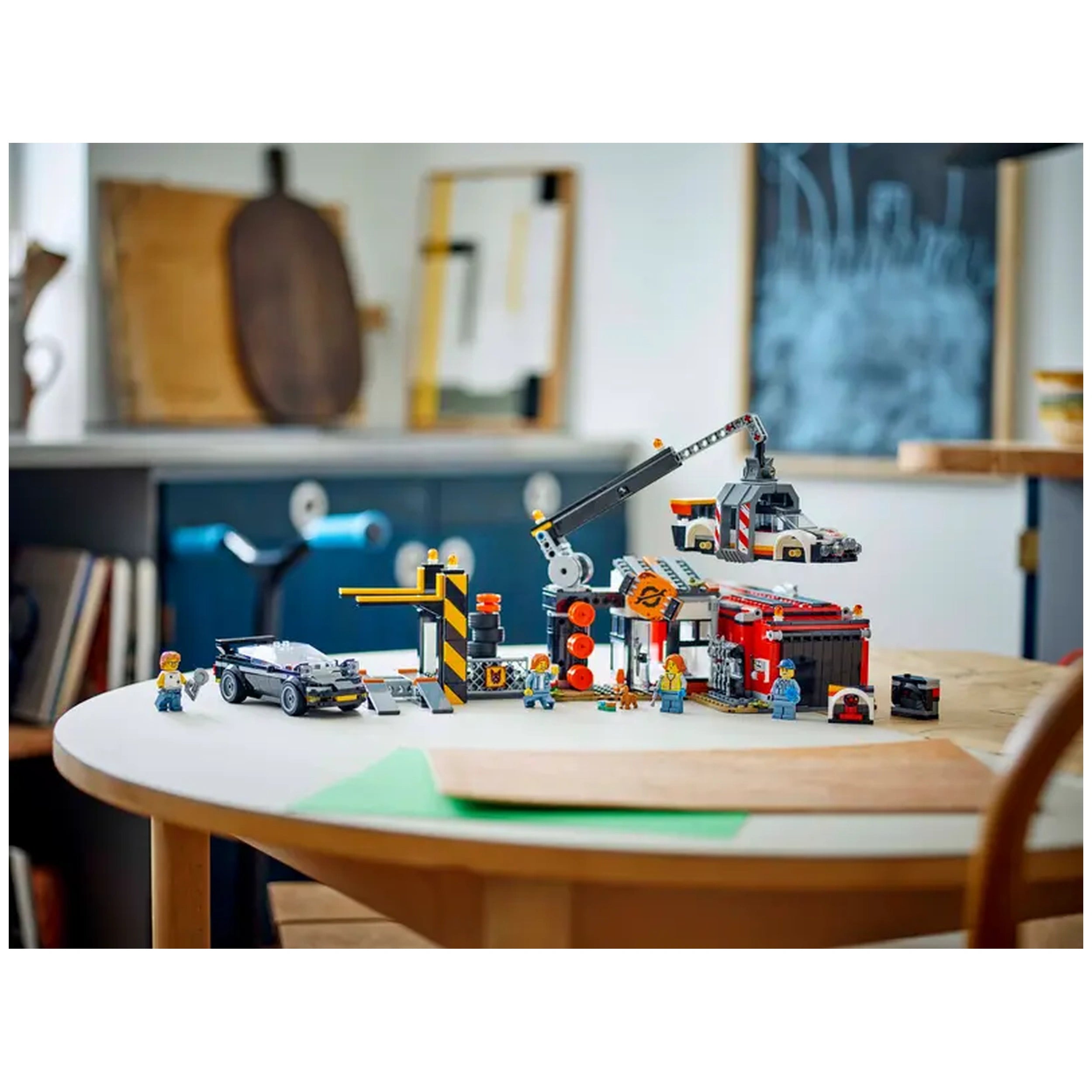 Colorful LEGO® City Scrapyard set displayed on a wooden table, featuring a claw crane, dismantled cars, and mini-figures interacting in a vibrant, educational environment.
