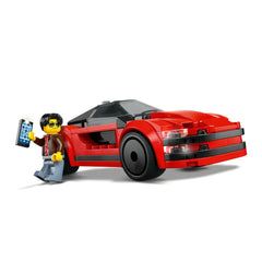 A red LEGO® sports car with black detailing and sleek curves, accompanied by a minifigure wearing sunglasses and holding a toy phone.