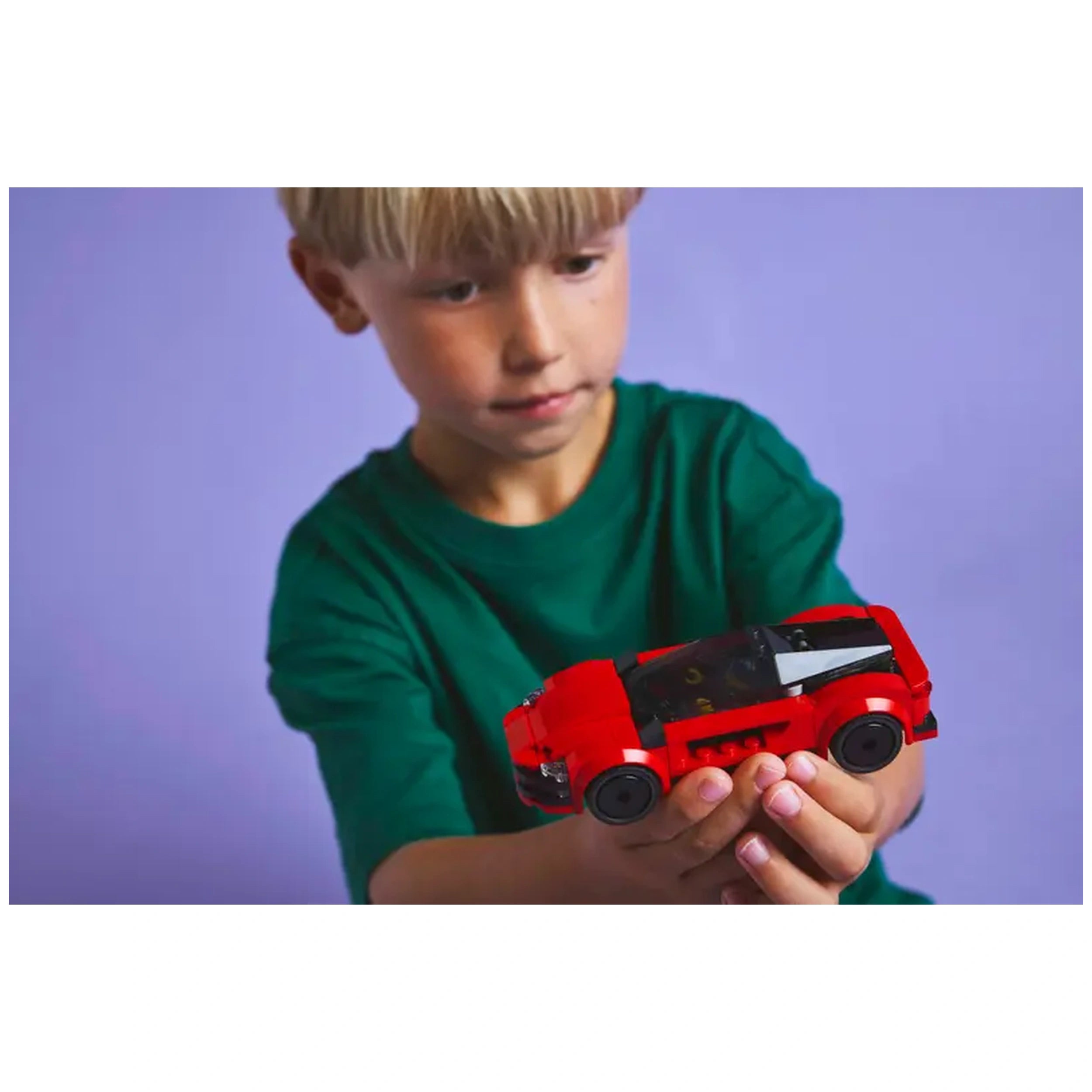 A boy in a green shirt holds a vibrant red LEGO® City Sports Car, showcasing its sleek design against a soft purple background.