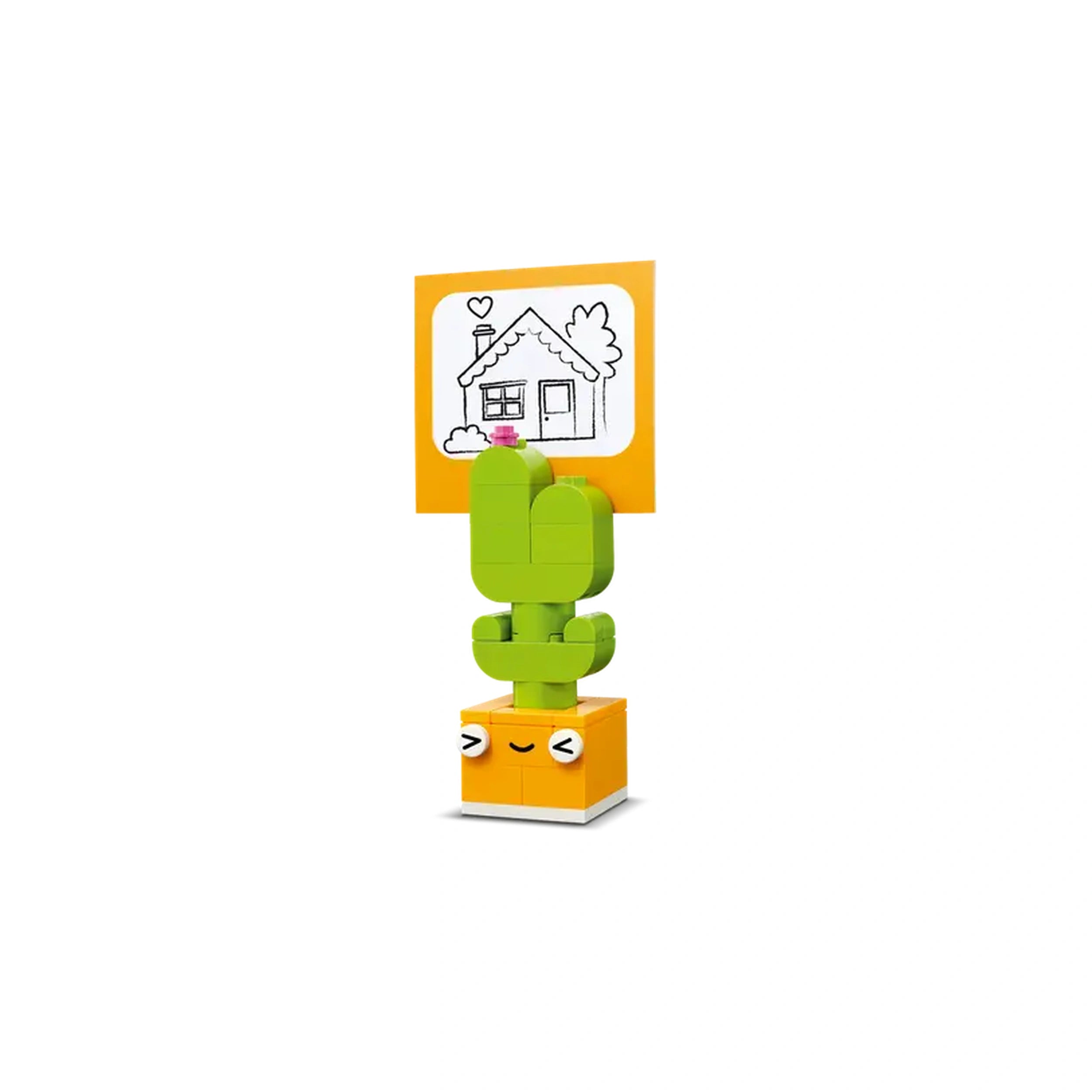 A vibrant LEGO® Creative Happy Box construction set featuring a playful green cactus figure with a smiling face, holding a yellow sign displaying a sketched house and clouds. The bright colors invite creativity and imaginative play.