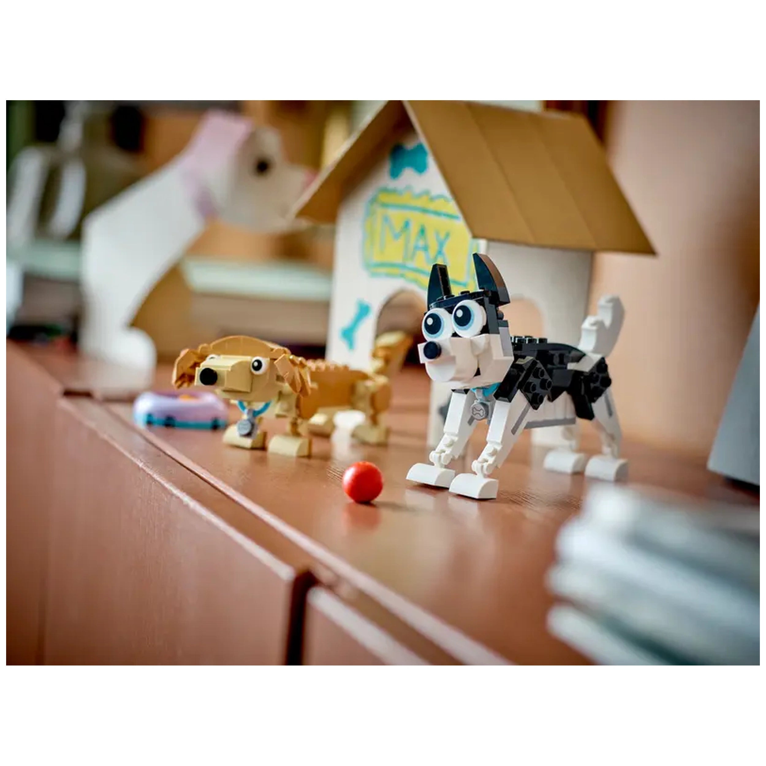 Three colorful LEGO dog models are displayed on a wooden surface. The black and white dog stands in a playful pose next to a brown dog, with a red ball nearby. A doghouse in the background features the name "MAX," adding a charming touch to the scene.