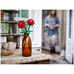LEGO® Creator Botanical - Roses set in an amber bottle, featuring two vibrant red roses with green leaves, on a rustic wooden table.
