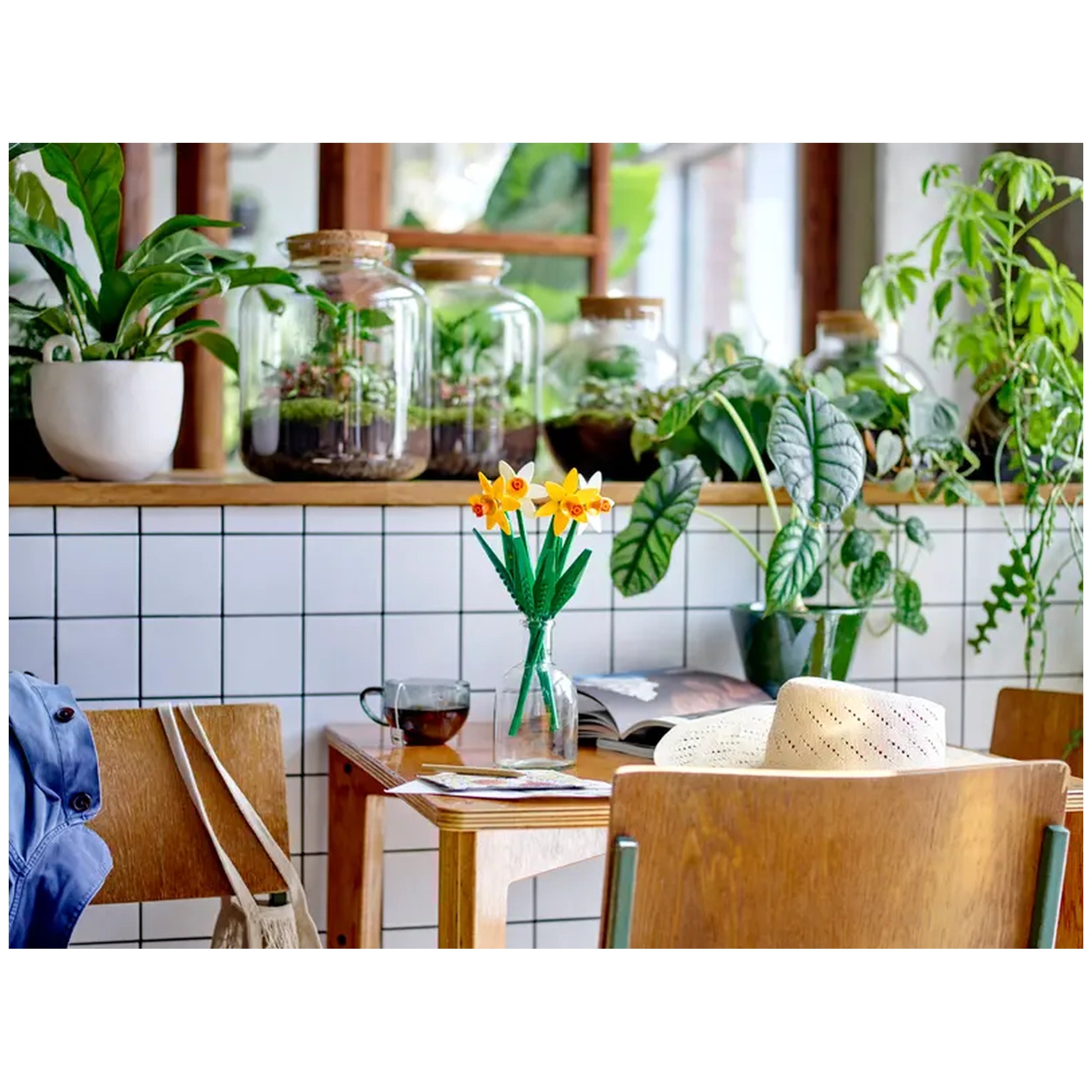 LEGO® Creator Daffodils construction set displayed on a wooden table, featuring two yellow and two white flowers in a vase, surrounded by green plants and a cup of tea.