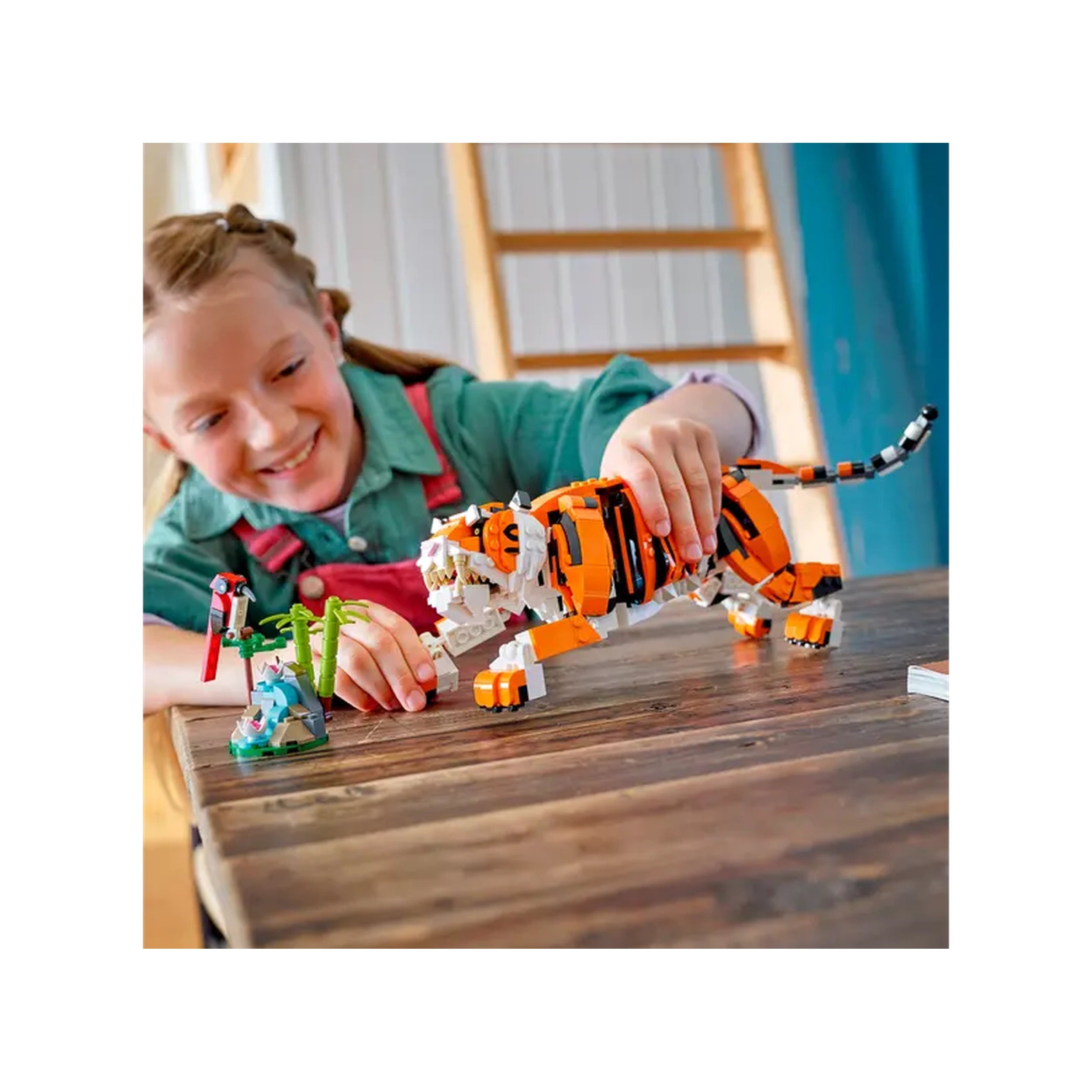 A child joyfully interacts with a vibrant LEGO® Majestic Tiger on a wooden table, showcasing the posable toy alongside a colorful bird and green foliage.