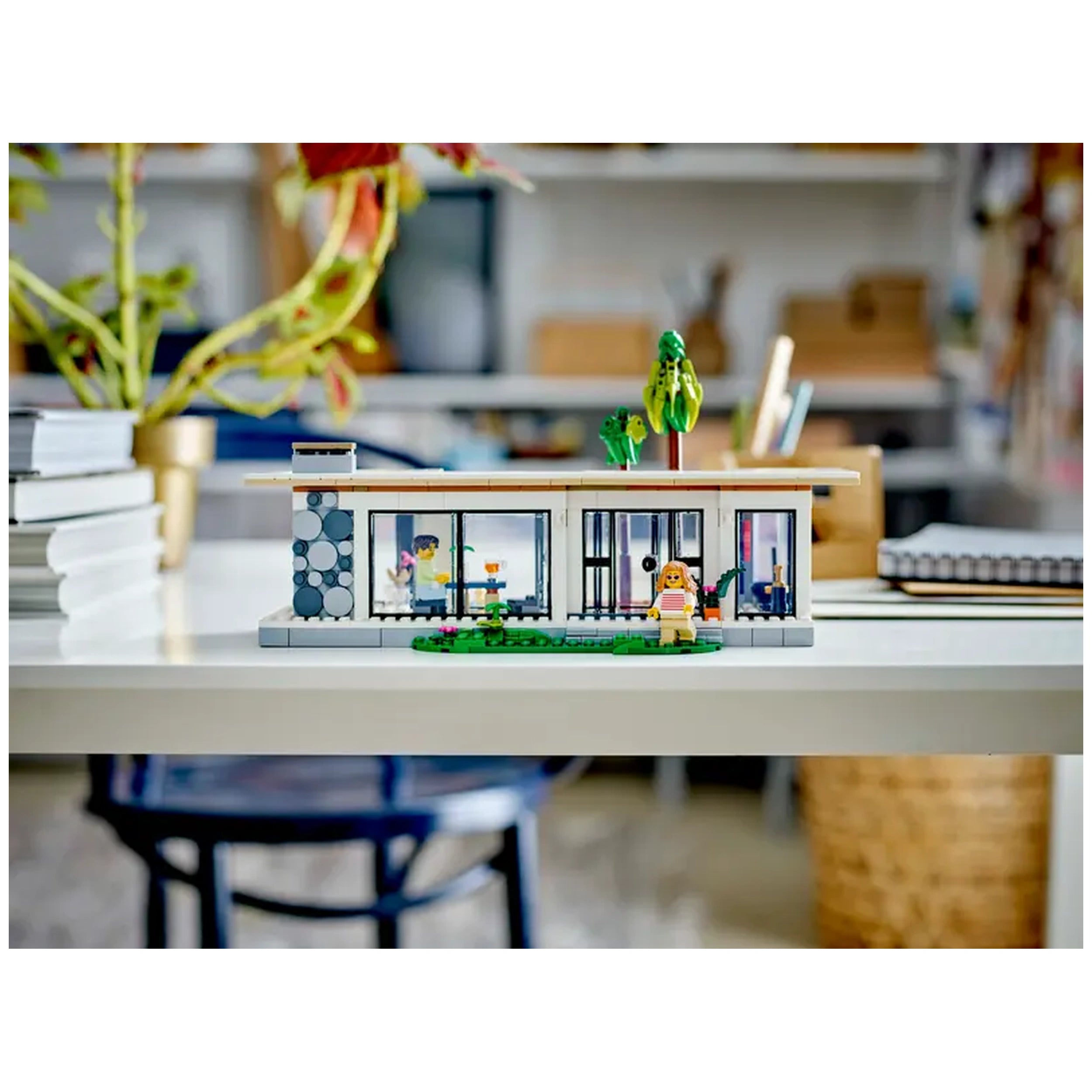 Modern LEGO Creator beach house model on a table, showcasing large windows, a garden with plants, and two mini-figures enjoying the outdoors.