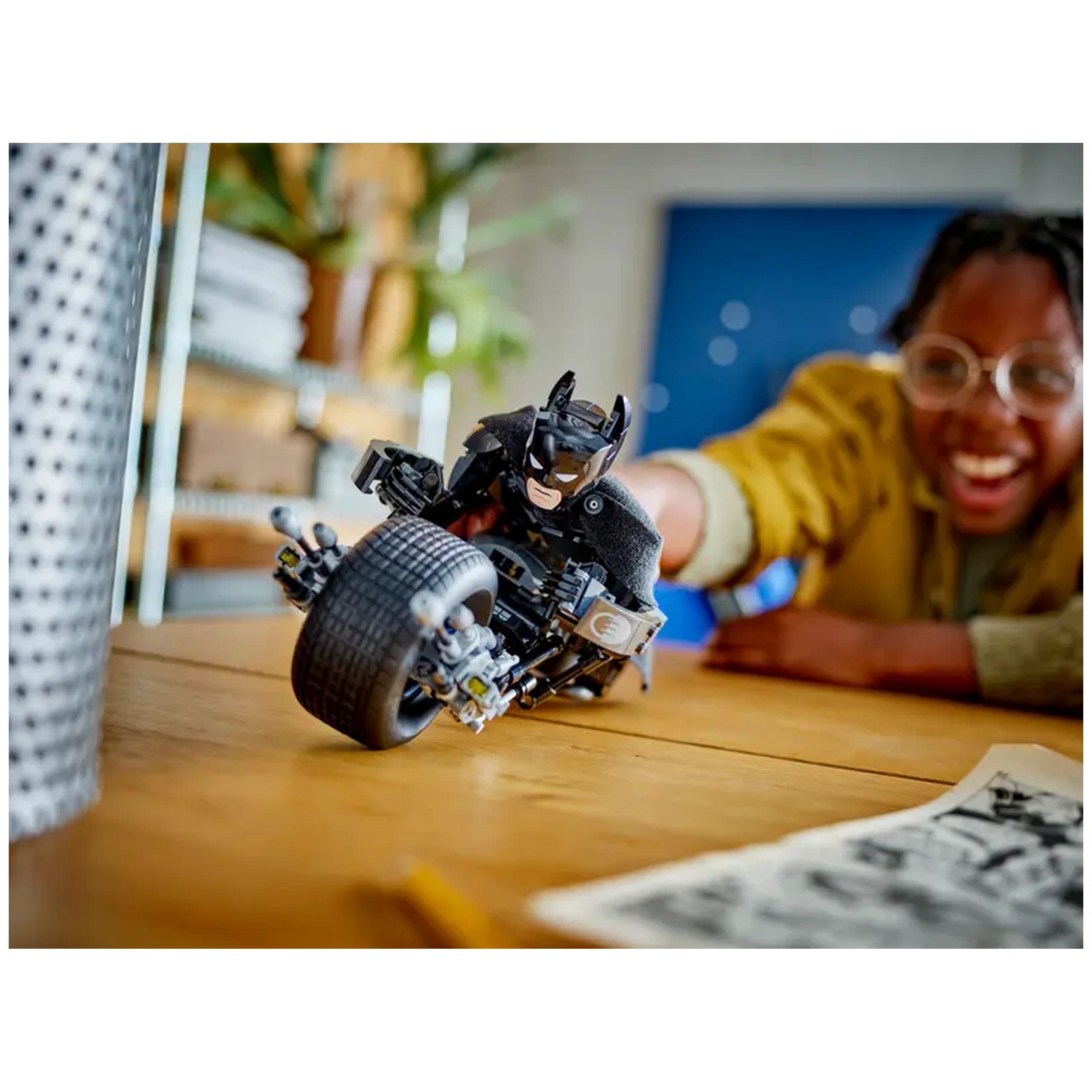 Batman construction figure riding the Bat-Pod bike, with a smiling child reaching out excitedly in a bright indoor setting.